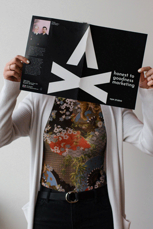 GIF of person holding a black TGW Studio brochure in front of their face