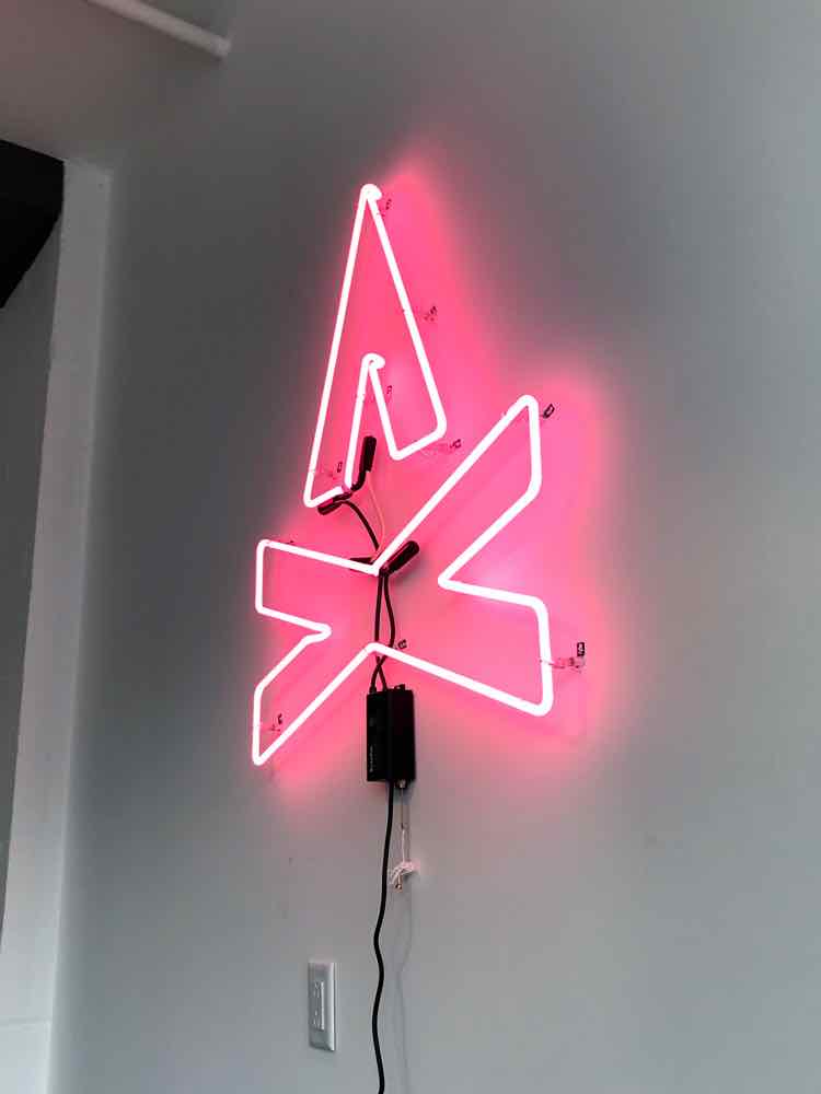 Photo of the TGW Studio neon sign, which features the TGW logo, a graphic representation of a campfire