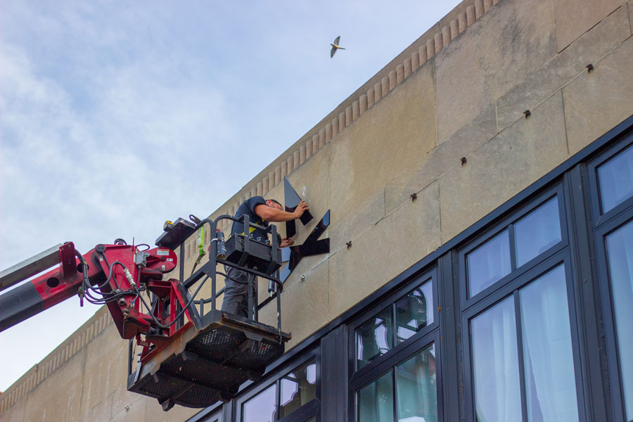 Person installing TGW Studio lettering on the exterior of the building. New-new