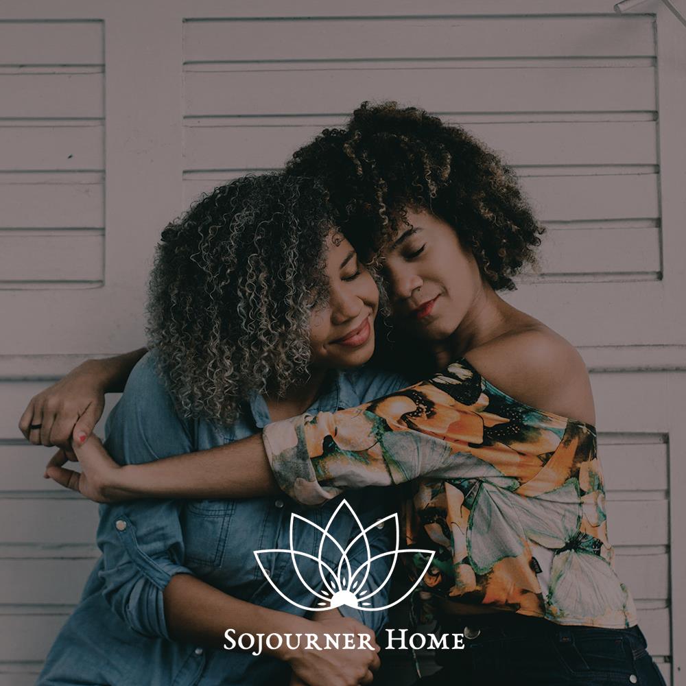 Photo of two women hugging in front of a white wall with text overlaid that says 'Sojourner Home'