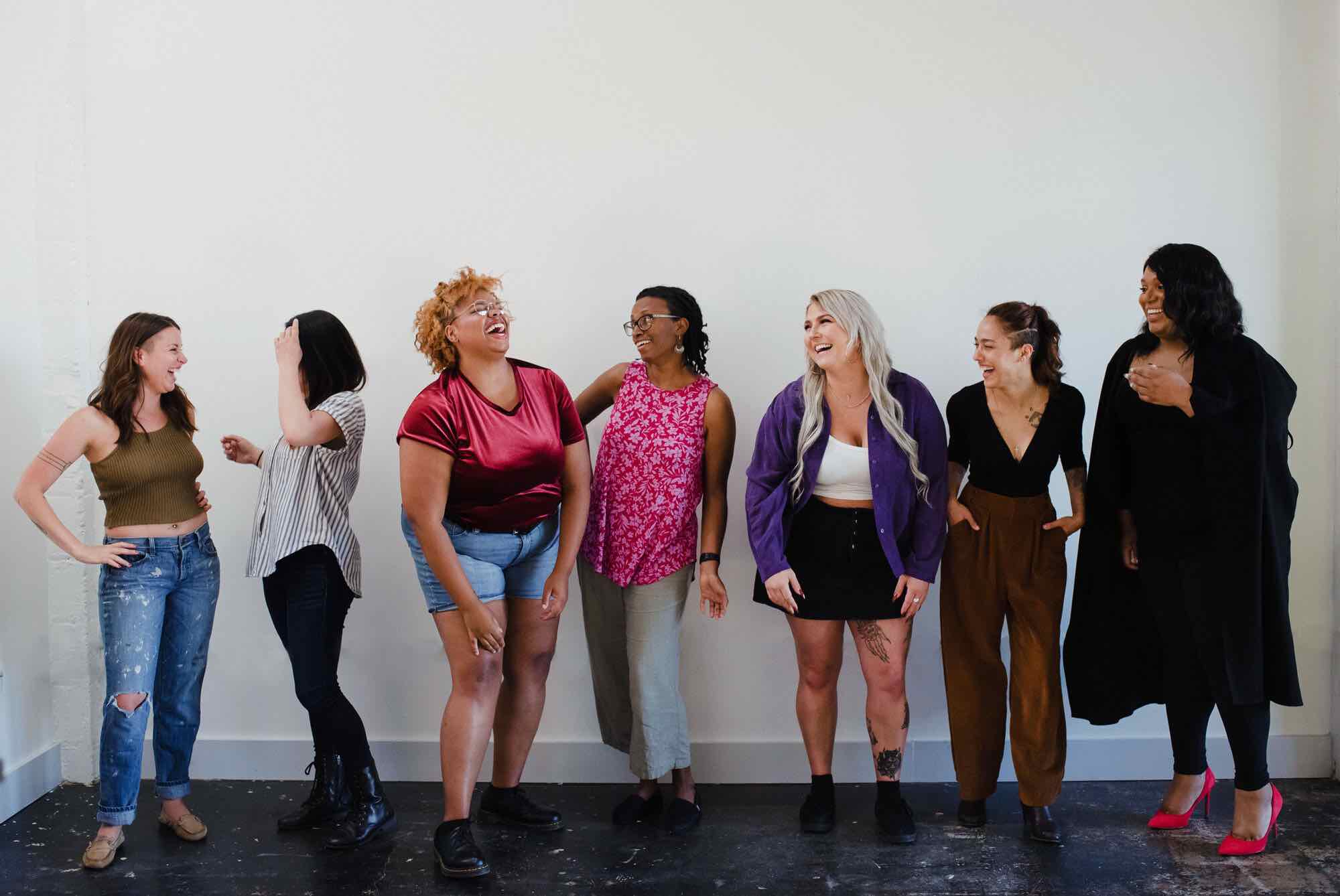 Photo of seven women laughing and smiling in front of a white wall as part of Trillium's Prep campaign