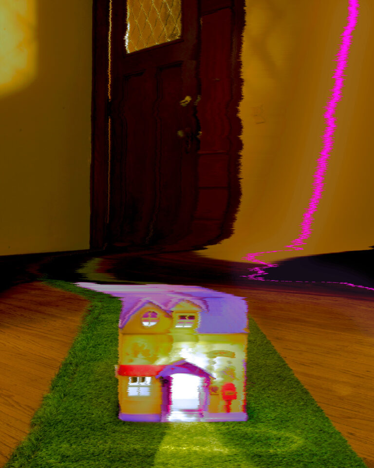 Digital photograph of a room-- on the floor is a colorful dollhouse with illuminated windows atop a green turf. The image is warped as if it was on an old television that was malfuctioning.