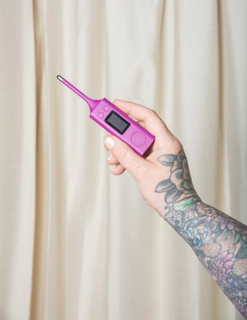 A tattooed hand holding a purple thermometer