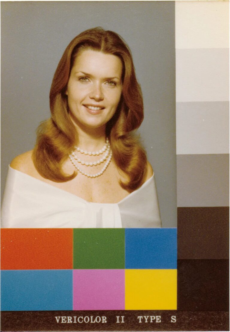 woman in white shirt and pearls poses for a portrait against a gray background
