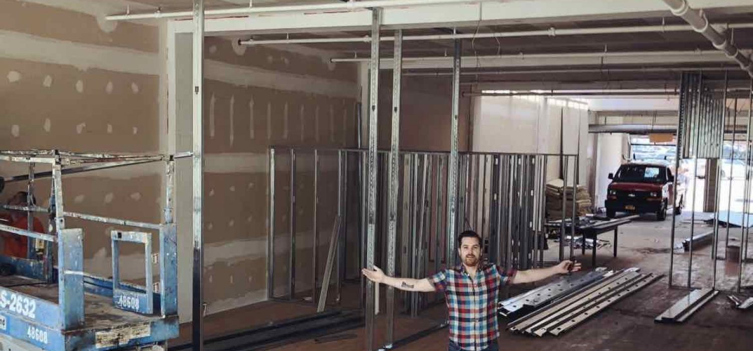 Interior of TGW Studio during the build out with a man standing in front with his arms out